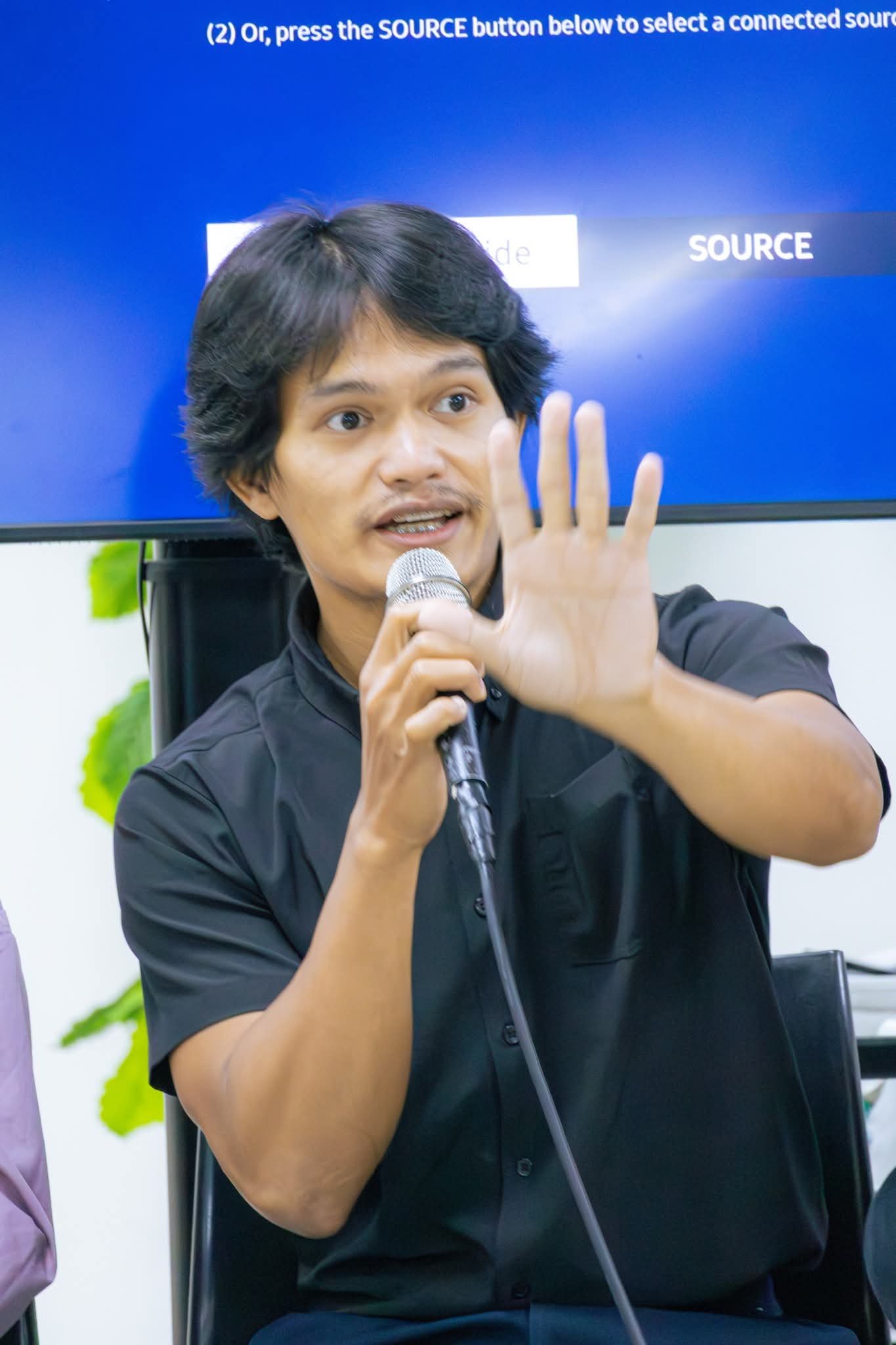 Jops speaking into a microphone during a presentation, gesturing while addressing the audience.